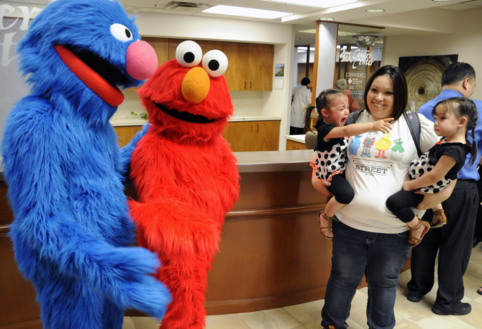 Elmo and Grover of Sesame Street Live frighten 2-year-old Gabriella Barbone, left, while being held by her mother, Andrea, center, along with her sister Avery, right, at the Tri-Cities Cancer Center Tuesday afternoon. The Sesame Streets Friends will be performing their "Make A New Friend" production on Wednesday at the Toyota Center.